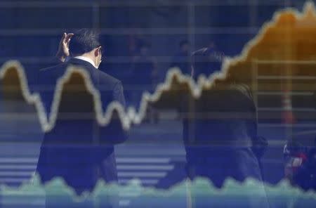 A man is reflected on an electronic board displaying a graph of Japan's Nikkei share average outside a brokerage in Tokyo March 12, 2015. REUTERS/Toru Hanai