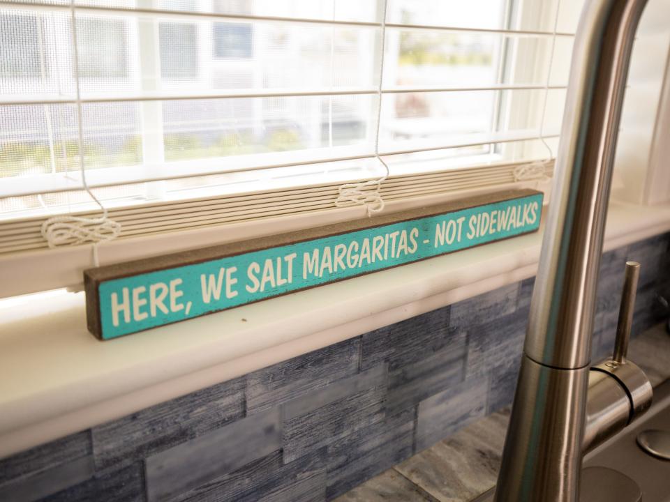 A sign that says "Here, we salt margaritas not sidewalks" under a window.