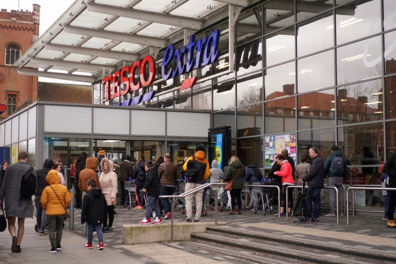 People queue outside of a supermarket before it opens, as the number of coronavirus cases grow around the world, in London