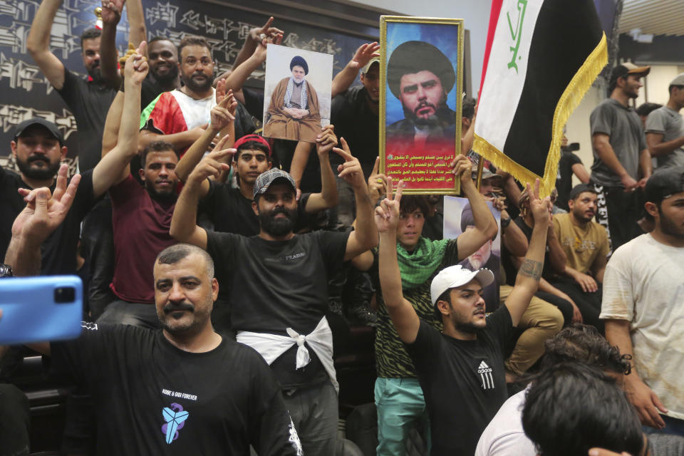 Iraqi protesters pose with national flags and pictures of Shiite cleric Muqtada al-Sadr inside the Parliament building in Baghdad, Iraq, Saturday, July 30, 2022. Thousands of followers of the influential Shiite cleric breached Iraq's parliament on Saturday, the second time in a week, to protest the government formation efforts lead by Iran-backed groups.(AP Photo/Anmar Khalil)