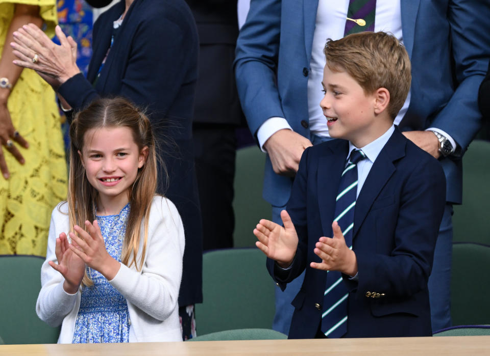 Princess Charlotte and Prince George are shown clapping in the audience, with Princess Charlotte wearing a dress and cardigan, and Prince George wearing a suit and tie