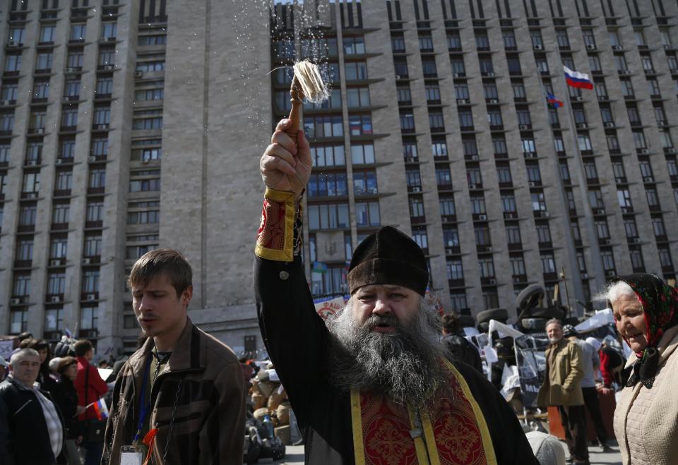 An Orthodox priest blesses people on the eve of Orthodox Easter, near barricades at the regional administration building that they had seized earlier in Donetsk, Ukraine, Friday, April 18, 2014. Pro-Russian insurgents in Ukraine’s east who have been occupying government buildings in more than 10 cities said Friday they will only leave them if the interim government in Kiev resigns.(AP Photo/Sergei Grits)