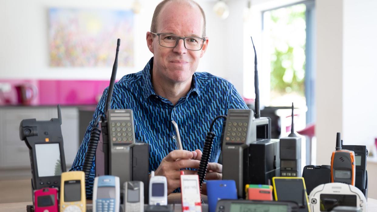 Auf dem vom Mobile Phone Museum herausgegebenen Foto sitzt Ben Wood, Gründer des Museums und Analyst des Unternehmens CCS Insight, hinter einigen der über 2.000 einzigartigen Mobiltelefone, die Teil des Online-Museums sein werden.
