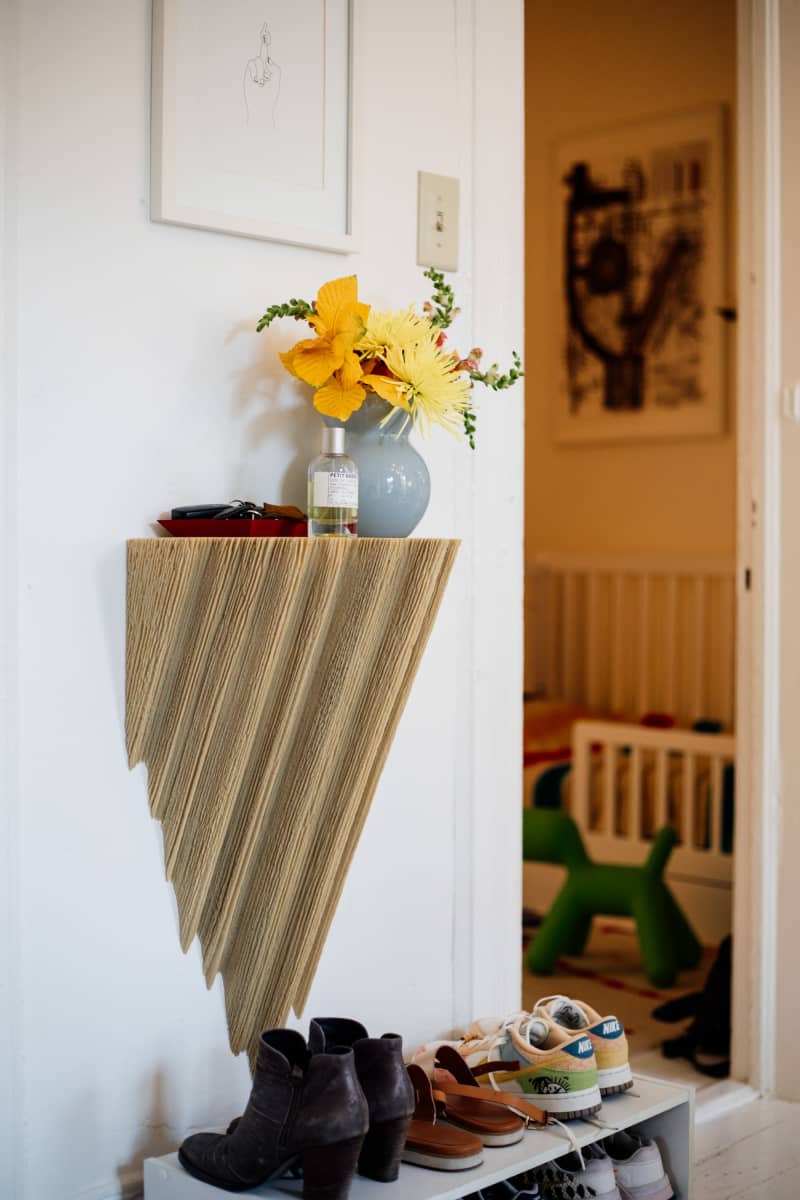 Room spray and floral arrangement on wooden shelf near apartment entrance.