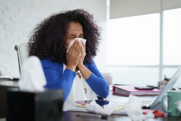 Woman blowing nose at desk