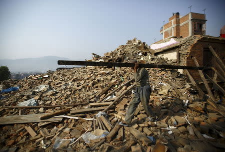 A man carrying a block of wood recovered from his house walks along the debris of collapsed houses, a month after the April 25 earthquake in Bhaktapur, Nepal May 25, 2015. REUTERS/Navesh Chitrakar