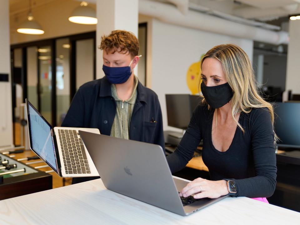 Two people wearing masks working together on laptops