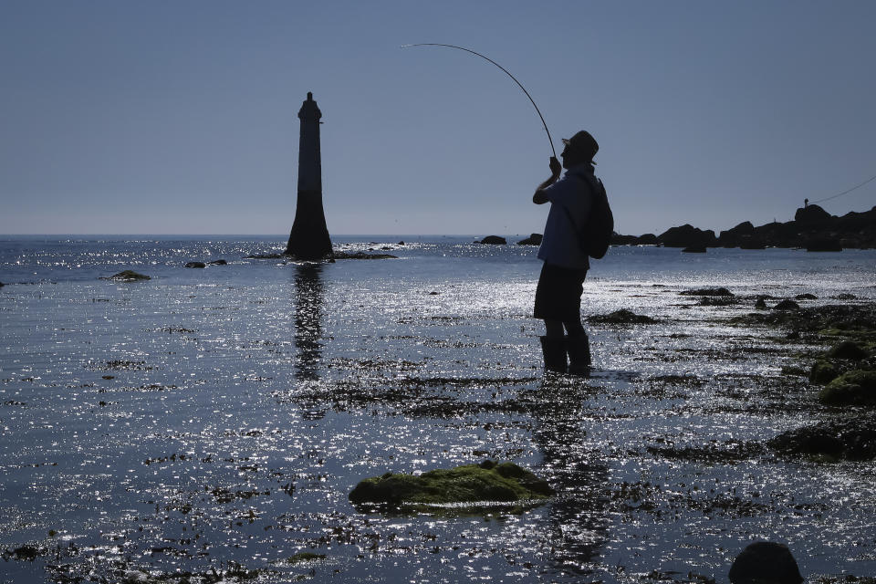 A man is silhouetted in the morning light as he fishes in the Teign estuary in Shaldon, Devon, England, Sunday July 18, 2021. Visiting the fishing village of Shaldon a small cluster of mainly Georgian houses and shops at the mouth of the River Teign, is like stepping back into a bygone era. It features simple pleasures that hark back to analog, unplugged summer days: a book and a picnic blanket, a bucket and spade, fish and chips.(AP Photo/Tony Hicks)