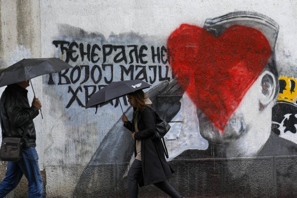 People walk by a mural of former Bosnian Serb military chief Ratko Mladic vandalized with red paint in Belgrade, Serbia, Monday, May 8, 2023. Mladic is serving a life sentence for genocide during the 1992-95 War in Bosnia but whom many Serbs still consider a hero. (AP Photo/Darko Vojinovic)