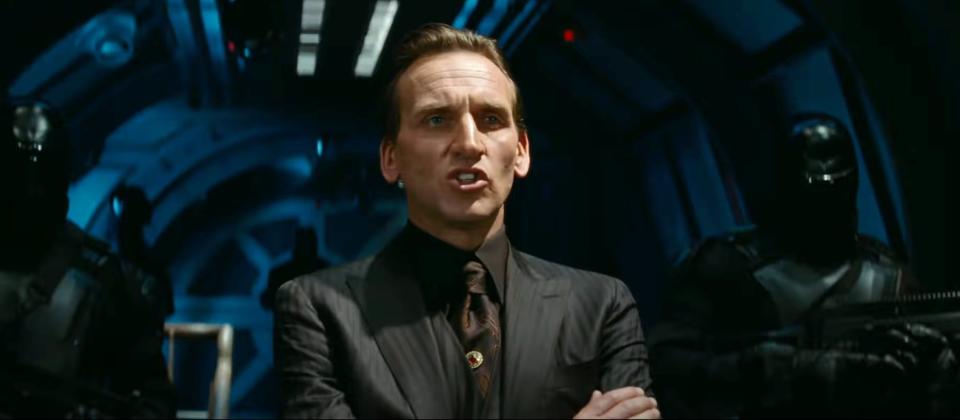 in a scene, Chris in a dark suit portrays a character in a futuristic control room setting