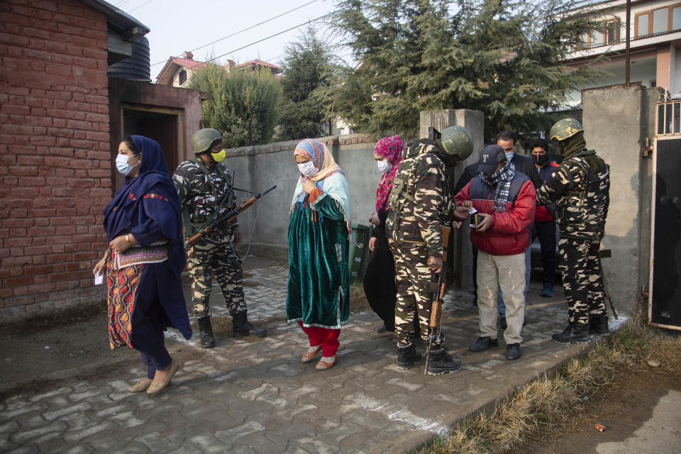 Soldiers stand guard as Kashmiris enter a polling booth area to cast their votes during the first phase of District Development Councils election on the outskirts of Srinagar, Indian controlled Kashmir, Saturday, Nov. 28, 2020. Thousands of people in Indian-controlled Kashmir voted Saturday amid tight security and freezing cold temperatures in the first phase of local elections, the first since New Delhi revoked the disputed region's semiautonomous status. (AP Photo/Mukhtar Khan)