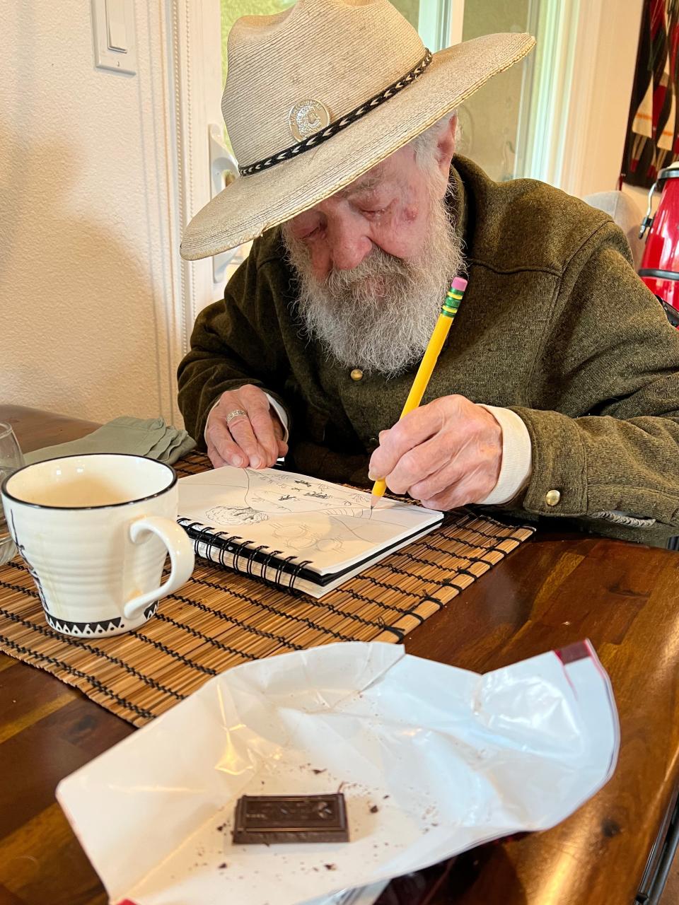 Uncle Jack drawing with a mug and some mostly-eaten dark chocolate in front of him.