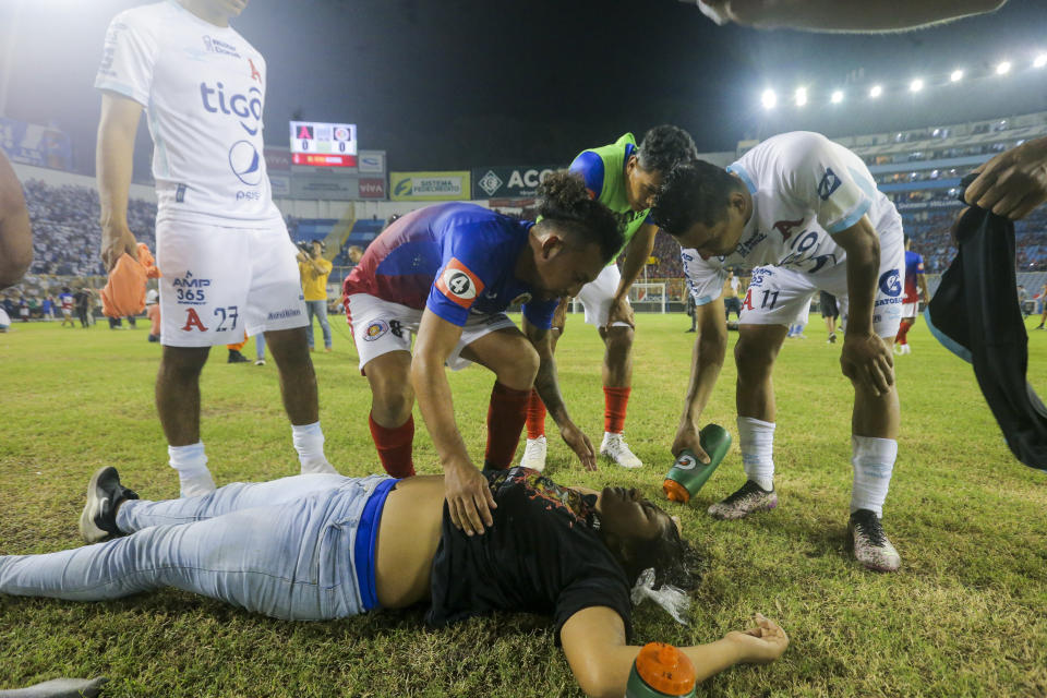 Soccer players attend a fan lying on the field of the Cuscatlan stadium in San Salvador, El Salvador, Saturday, May 20, 2023. At least nine people were killed and dozens more injured when stampeding fans pushed through one of the access gates at a quarterfinal Salvadoran league soccer match between Alianza and FAS. (AP Photo/Milton Flores)