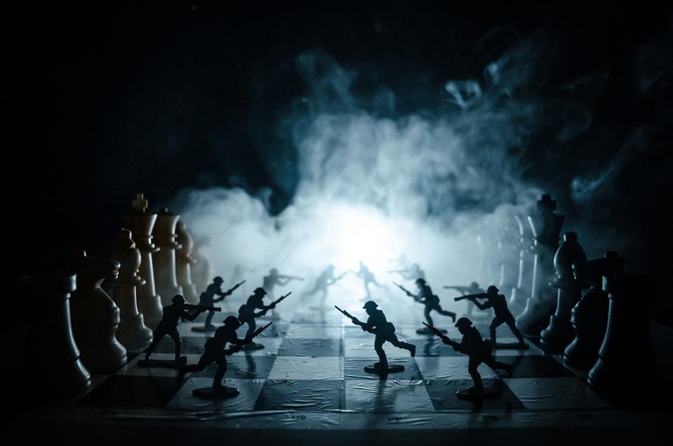 Plastic army men on a chess board with smoke billowing behind them.