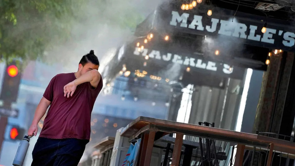 PHOTO: In this July 13, 2023, file photo, a man wipes his face as he walks under misters in downtown Phoenix. (Matt York/AP, FILE)