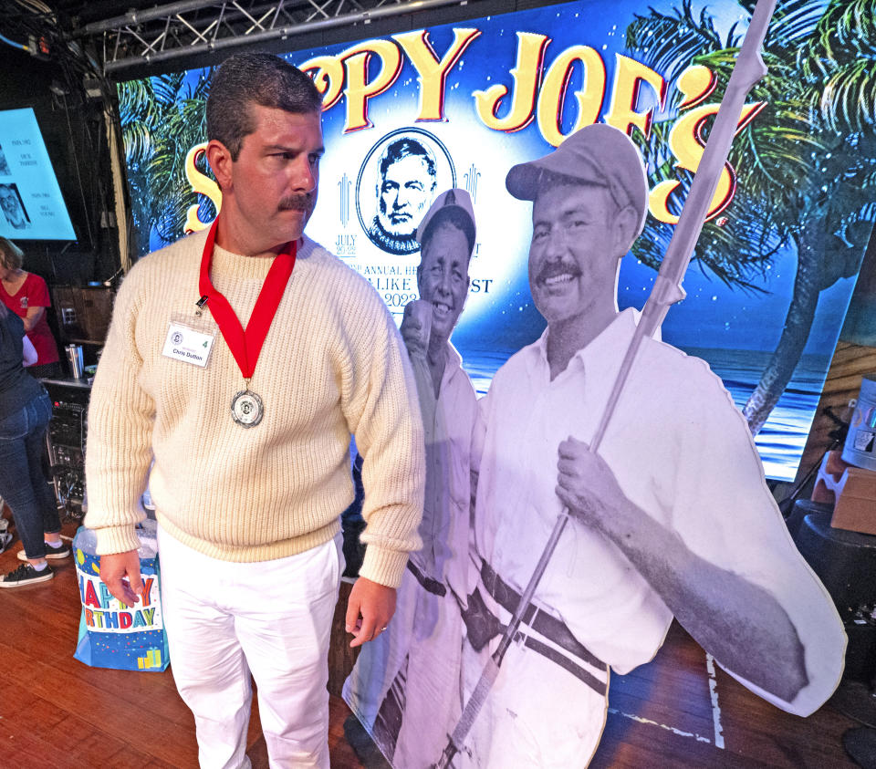 In this Saturday, July 22, 2023, photo provided by the Florida Keys News Bureau, Chris Dutton gazes at a photograph of Ernest Hemingway taken while the author lived in Key West during the 1930s as he competes in the Hemingway Look-Alike Contest at Sloppy Joe's Bar in Key West, Fla. The competition was a highlight of the annual Hemingway Days festival that ends Sunday, July 23. Dutton made the finals as a young Hemingway look-alike but did not win. (Andy Newman/Florida Keys News Bureau via AP)