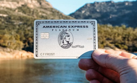 A person holding an American Express credit card with a lake in the background.