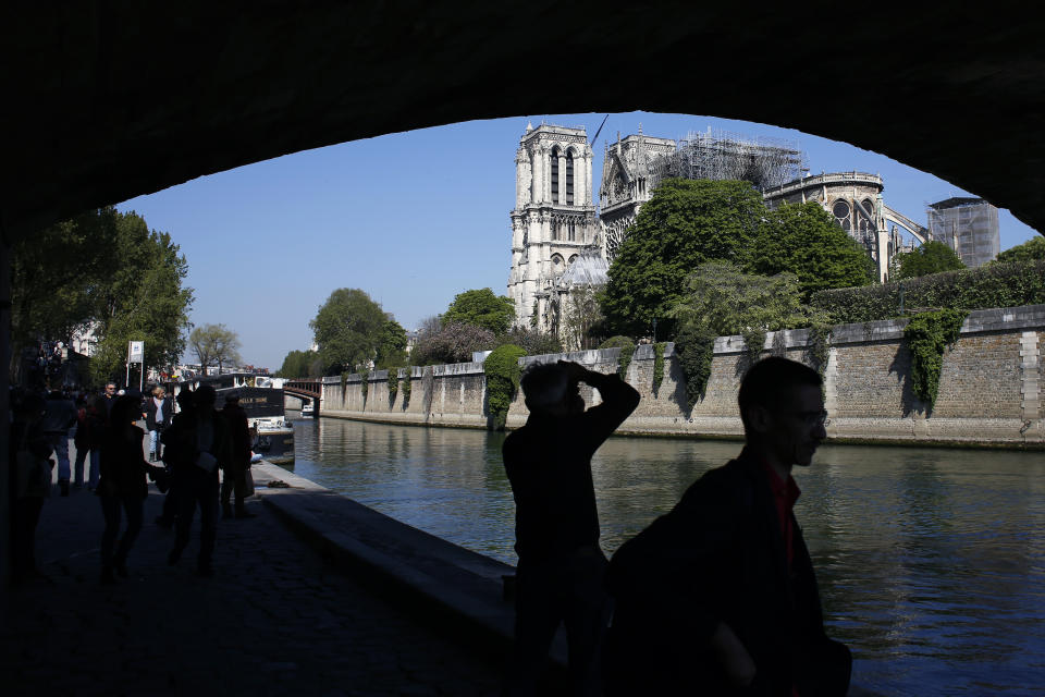 Tourists walk nearby Notre Dame cathedral, in Paris, Friday, April 19, 2019. Rebuilding Notre Dame, the 800-year-old Paris cathedral devastated by fire this week, will cost billions of dollars as architects, historians and artisans work to preserve the medieval landmark. (AP Photo/Thibault Camus)