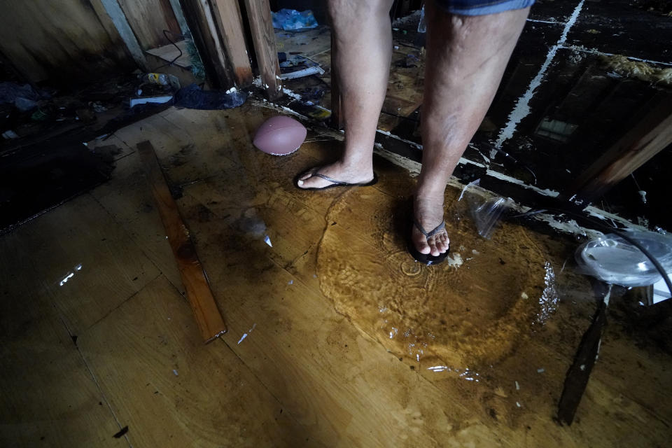 Standing water from roof holes splashes on the plywood sub-floor as Irene Verdin talks inside her home that was heavily damaged by Hurricane Ida nine months before, along Bayou Pointe-au-Chien, La., Tuesday, May 24, 2022. (AP Photo/Gerald Herbert)