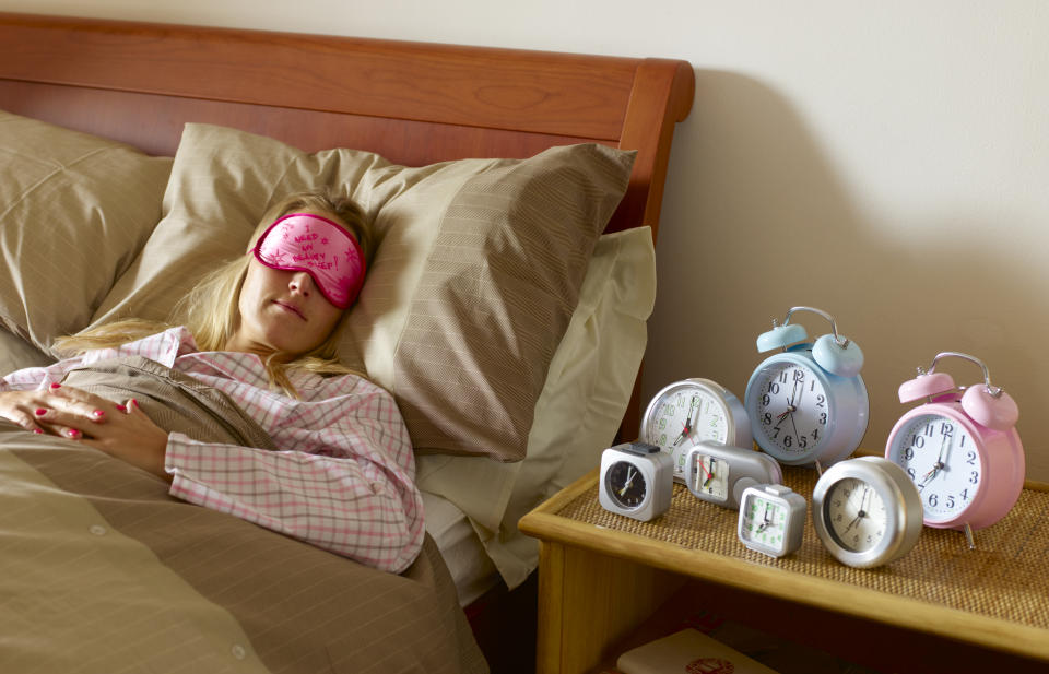 woman lying in bed with seven alarm clocks on her nightside table.