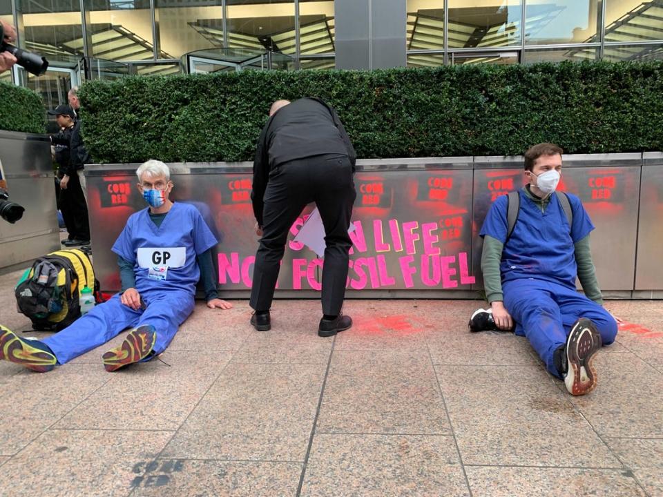 A police officer removes sticky notes put up by XR as two GPs sit glued to the ground outside JP Morgan’s building (The Independent)