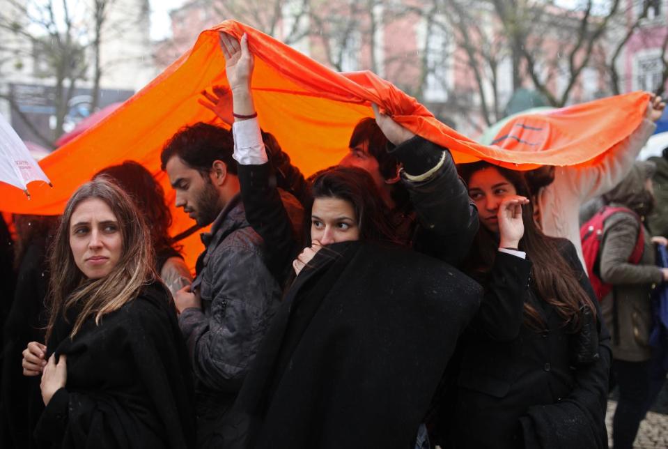In this picture shot April 2 2014, students protect themselves from the rain while protesting cuts in education in Lisbon. For most Portuguese under 50 years old, the revolution is a milestone they learned about at school. But with youth unemployment at 35 percent, the anniversary has struck a chord with many young people. Nationwide commemorations include dozens of protest events organized on social media. (AP Photo/Francisco Seco)