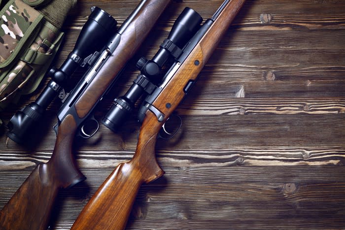 Two hunting rifles with mounted scopes lying on a wooden floor.