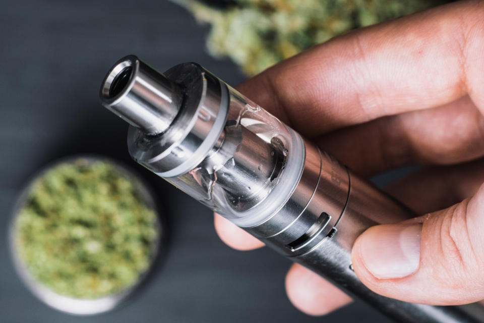 Marijuana Bud Cannabis In Glass Jar With Oil Extract Vape Pen On Black Background. Selective Focus With Copy Space. Grinder and marijuana cannabis weed