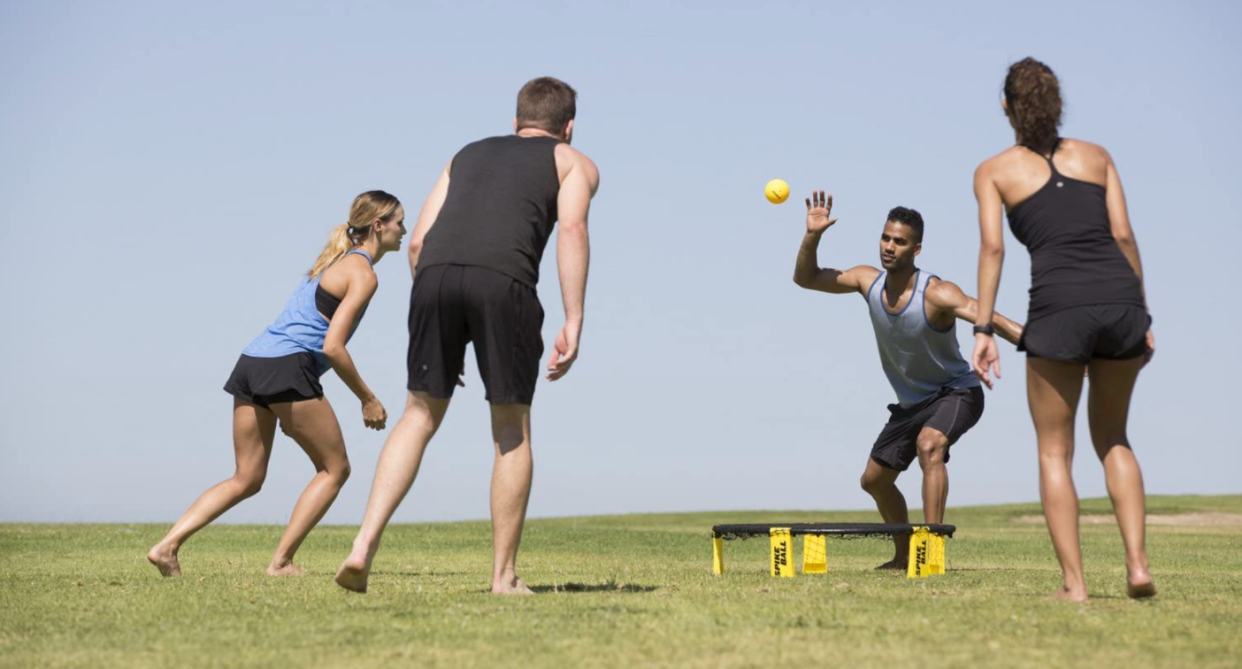 spikeball, fours friends in workout apparel playing spikeball with yellow ball on grass outside