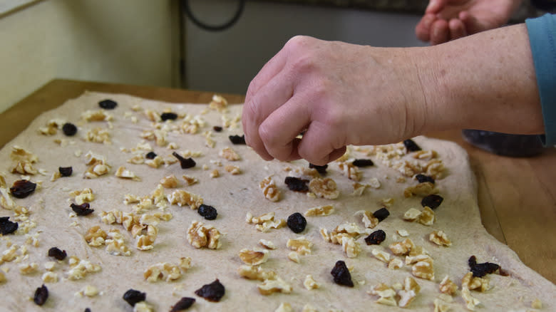 hand sprinkling nuts and fruits onto bread dough
