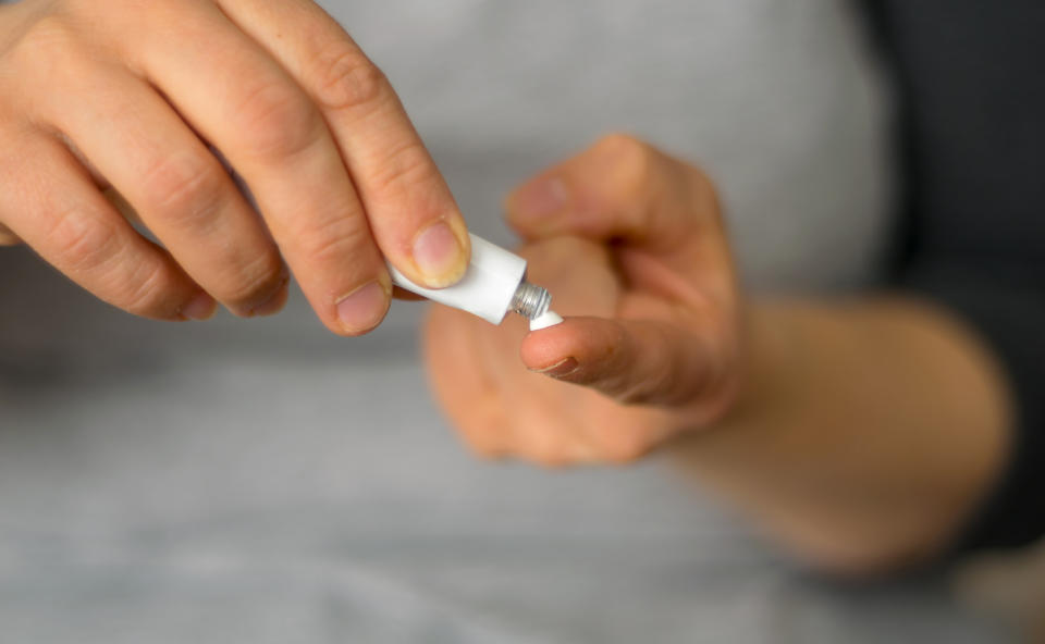 A person applying ointment from a small tube onto their finger