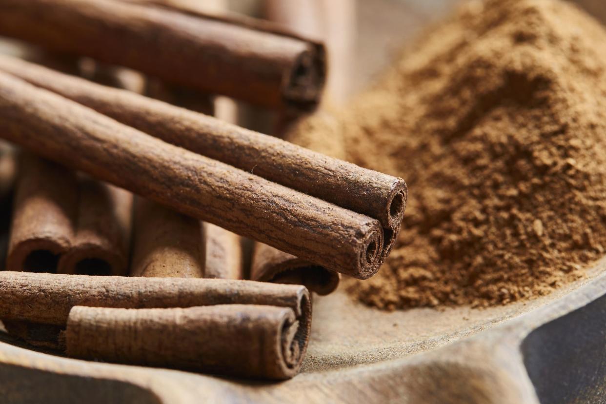 Cinnamon sticks and powder in a handmade wooden bowl, on a kitchen table, baking preparation, macro shot with a copy space