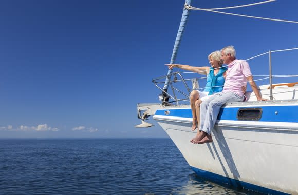 A senior man and woman sit on a sailboat that's on the water.