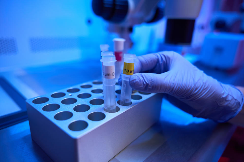 Man in protective glove takes out test tube with biomaterial from the cell of special box, tubes are marked