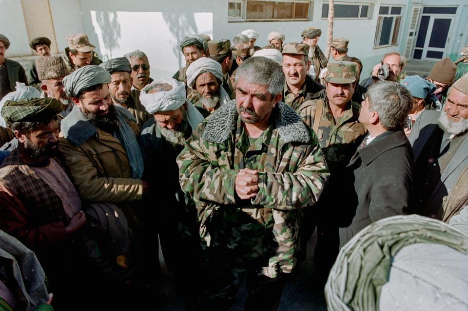 A commander addresses soldiers who stand around him.