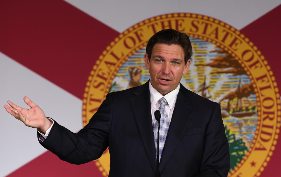 Florida Gov. Ron DeSantis stands at a microphone in front of a backdrop of Florida's state flag.