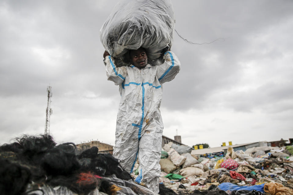 A man wearing a protective suit he found in the trash scavenges for artificial hair at Dandora, the largest garbage dump in the Kenyan capital of Nairobi, Sunday, March 28, 2021. Trash pickers, who are not eligible for the COVID-19 vaccine, say the gear protects them from the weather during the rainy season. (AP Photo/Brian Inganga)