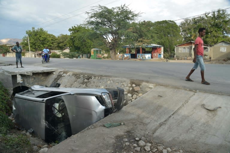 A car damaged by a bus lies on the side of a road in Gonaives