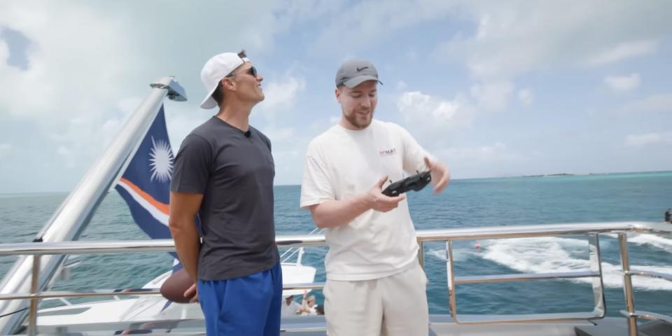 Tom Brady and MrBeast controlling a drone on the deck of a yacht.