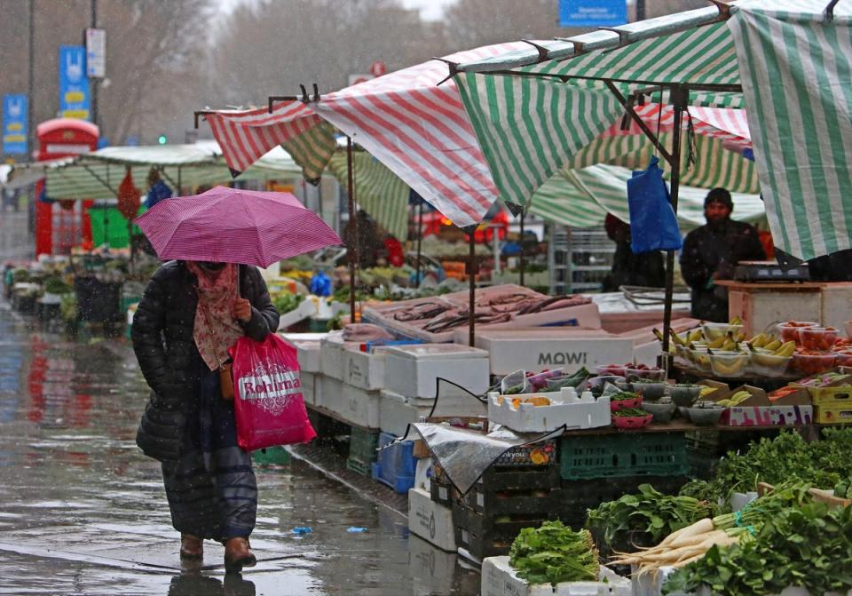 A pedestrian shelters from the rain as they walk past fruit and vegetable at a market stall in east London (AFP via Getty Images)