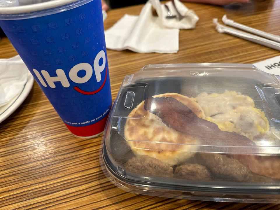 Ihop to-go cup next to plastic container of biscuits, sausage, and bacon