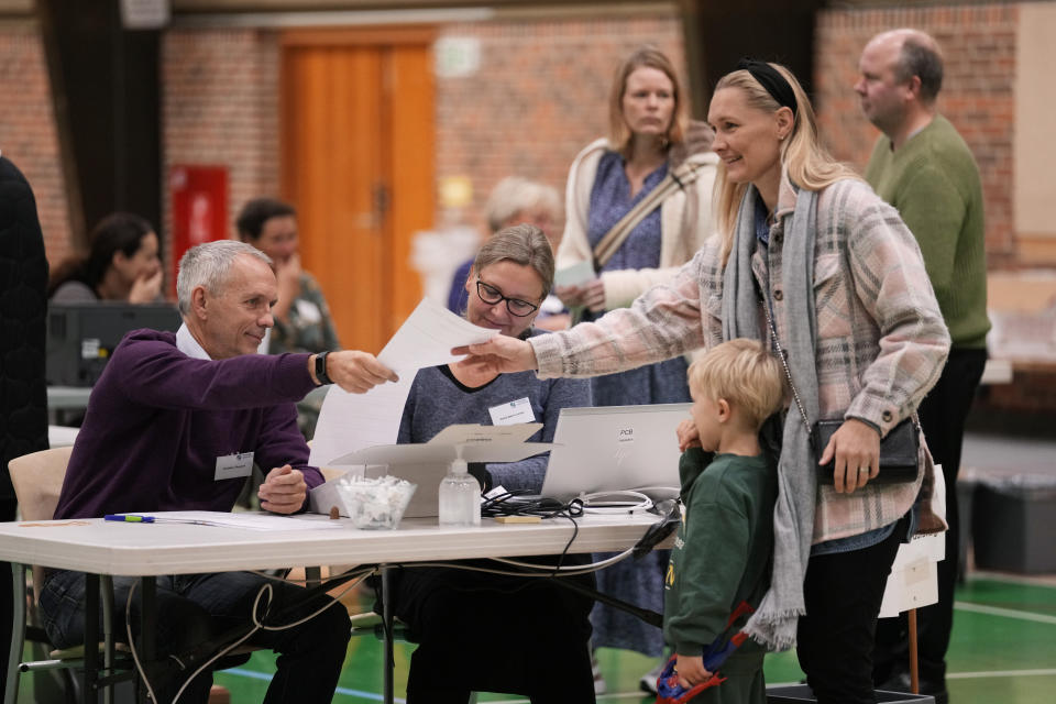 A woman with a child receives a ballot at a polling station in Hareskovhallen in Vaerloese, Denmark, on Tuesday, Nov 1, 2022. Denmark's election on Tuesday is expected to change its political landscape, with new parties hoping to enter parliament and others seeing their support dwindle. A former prime minister who left his party to create a new one this year could end up as a kingmaker, with his votes being needed to form a new government. (AP Photo/Sergei Grits)