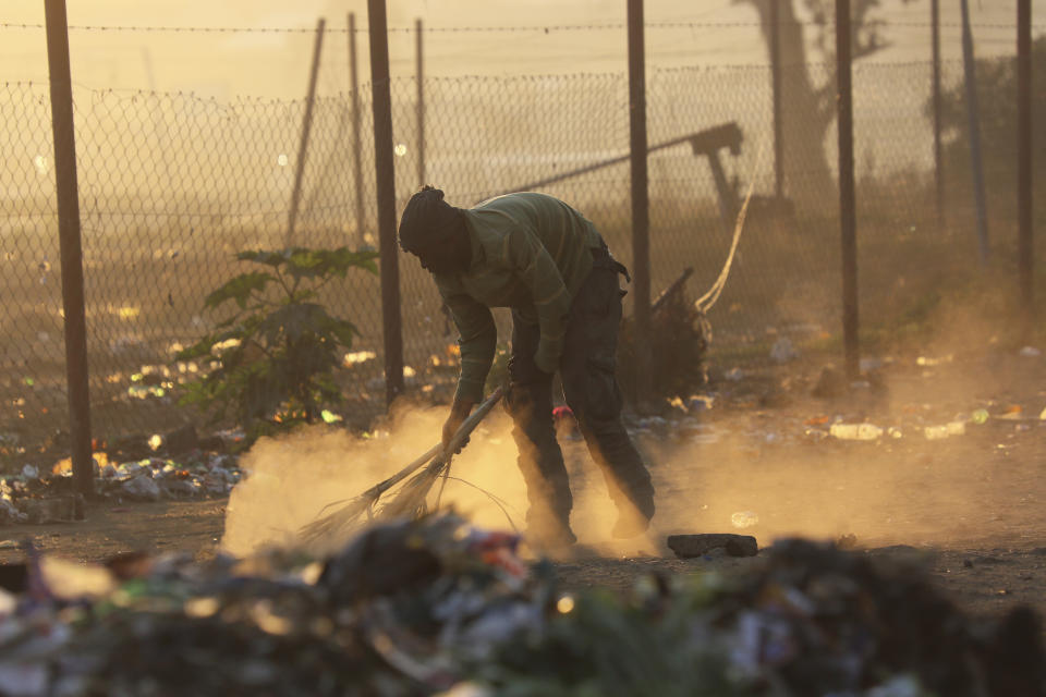 A man sweeps a path near a dumpsite in Harare, Thursday, Aug, 8, 2019. Many Zimbabweans who cheered the downfall of longtime leader Robert Mugabe two years ago now find the country's economy even worse than before.(AP Photo/Tsvangirayi Mukwazhi)