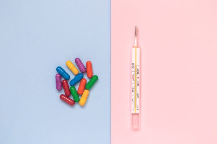 A pile of brightly colored pill capsules next to a thermometer.