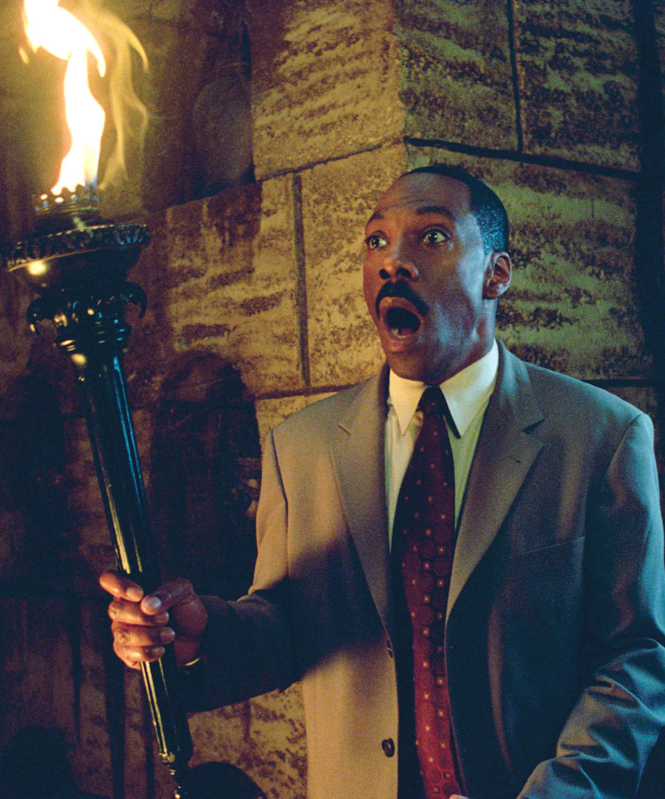 Eddie Murphy in a scene from "The Haunted Mansion," holding a lit torch with an expression of surprise