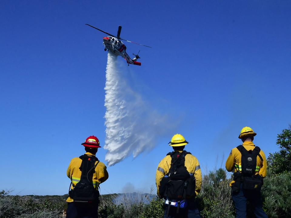 Firefighters watch a helicopter drop water on the flames.