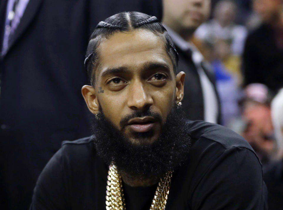 FILE - This March 29, 2018 file photo shows rapper Nipsey Hussle at an NBA basketball game between the Golden State Warriors and the Milwaukee Bucks in Oakland, Calif. Hussle, who was shot and killed outside of his clothing store in Los Angeles on March 31, 2019, received three Grammy nominations on Wednesday, Nov. 20. His song “Racks In the Midldle is up for best rap performance and best rap song, while “Higher,” a collaboration with DJ Khaled and John Legend that one of the last songs Hussle recorded, is nominated for best rap/sung performance.. (AP Photo/Marcio Jose Sanchez, File)