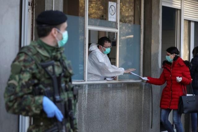 A medical worker takes papers from a woman at the infection clinic as the number of coronavirus (COVID-19) cases grow around the world in Belgrade