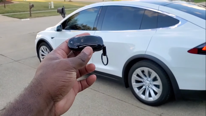 A photo of someone holding a Tesla Model X key fob in front of a Model X