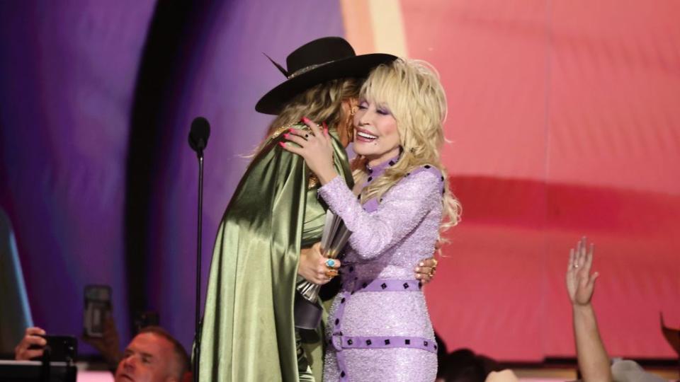 lainey wilson wearing gold outfit hugs dolly parton in light purple gown onstage at 58th acm awards